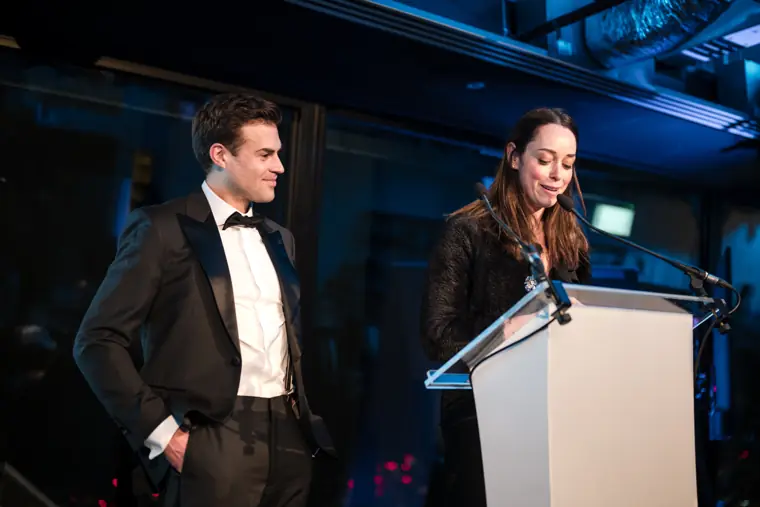 Two presenters speaking on stage.