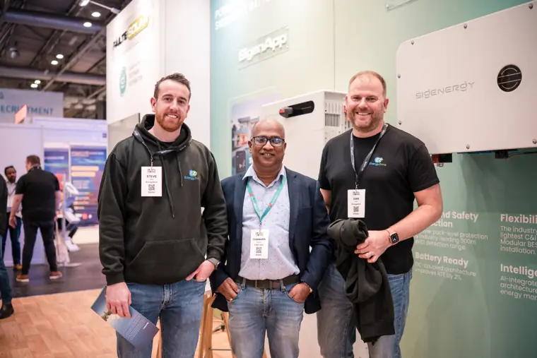 Three attendees photographed in front of the product wall.