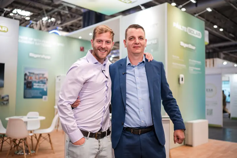 Two attendees photographed in front of the booth.