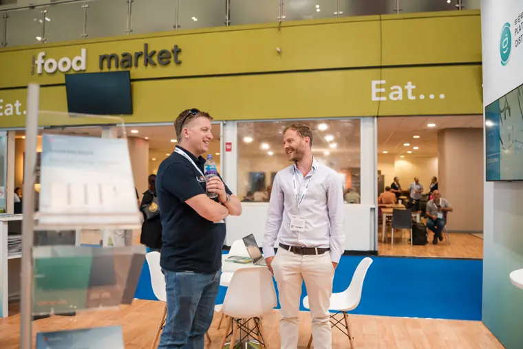 Two visitors meet beside the exhibition food area.
