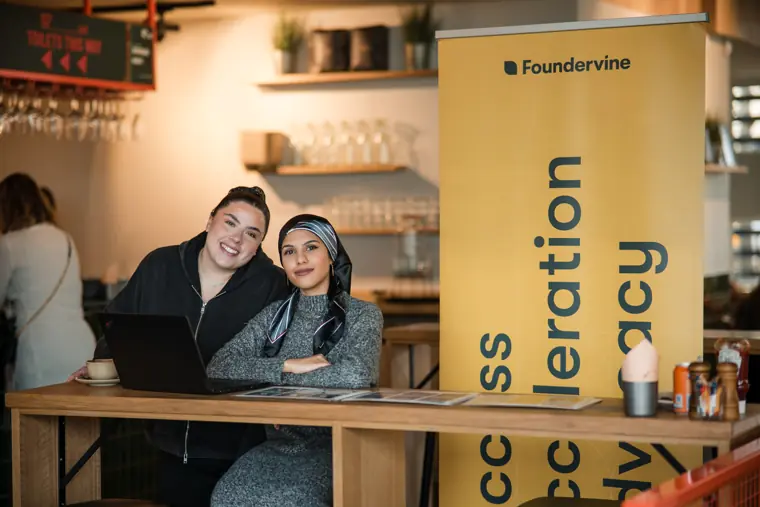 Two organisers smile beside the Foundervine welcome banner.