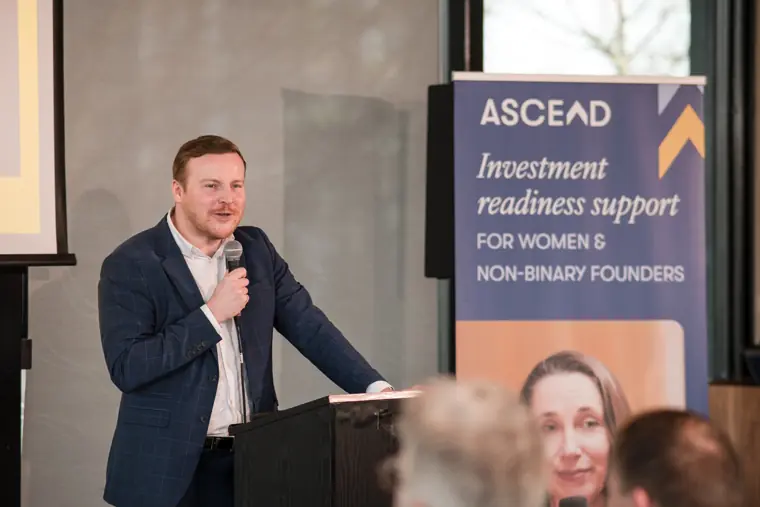 A speaker addresses the room beside the Ascend banner.