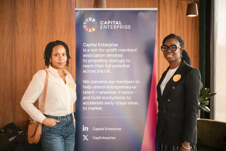 Two guests pose in front of the Capital Enterprise banner.