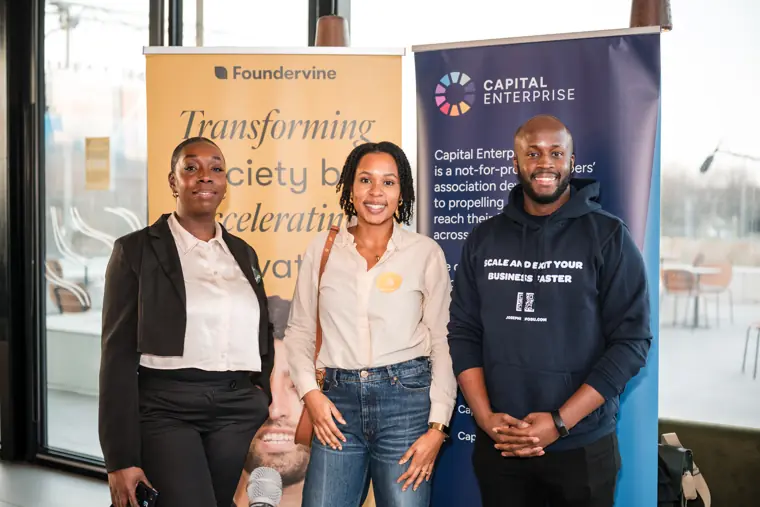 Three attendees pose in front of the Foundervine and Capital Enterprise banners.