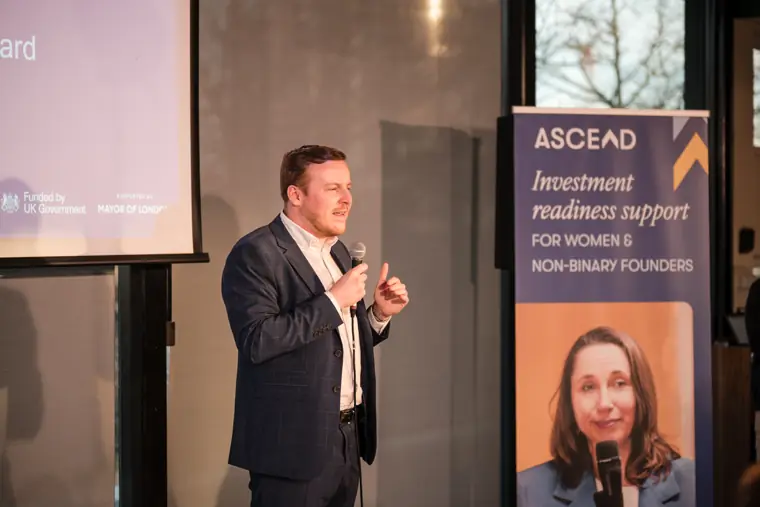 A speaker discusses the programme beside the Ascend sign.