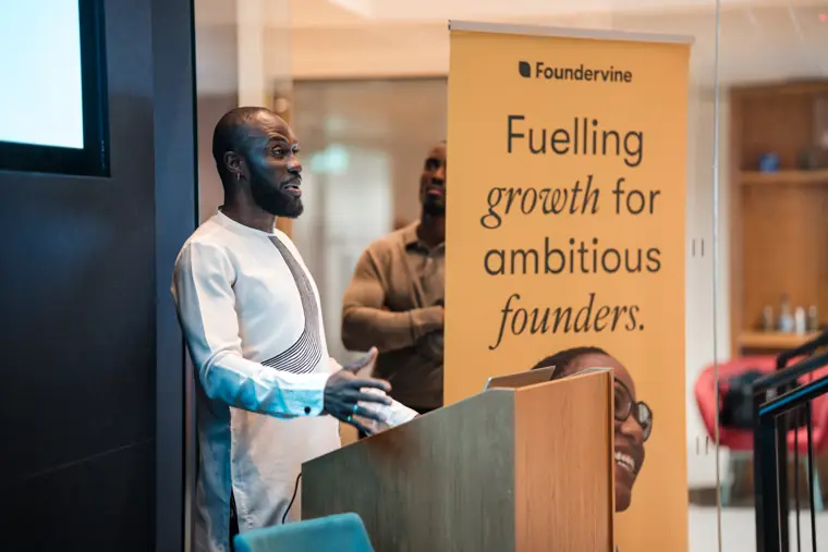 A speaker addresses the room beside Foundervine branding.