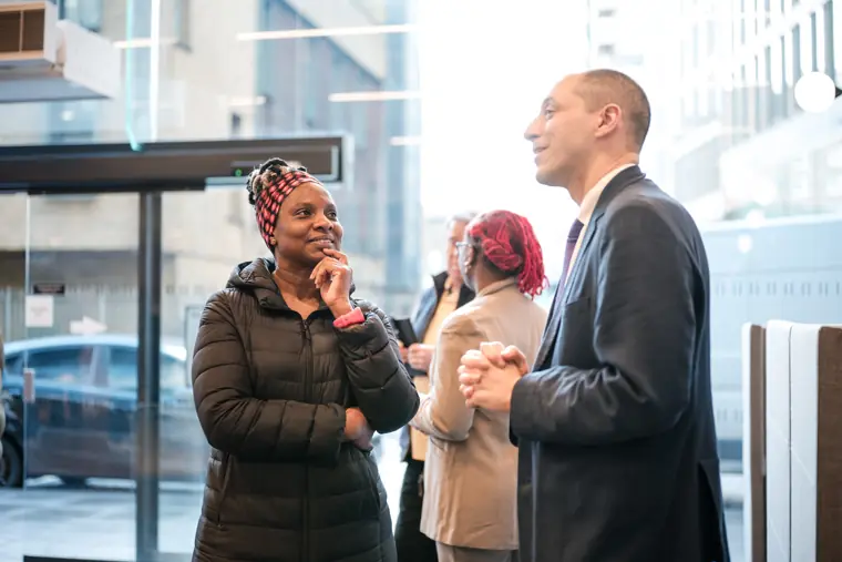 A guest greets another participant by the windows.