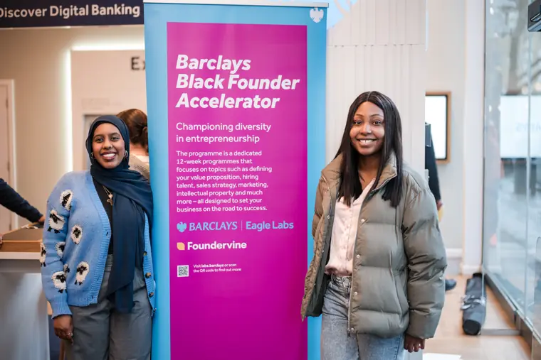 Two attendees pose beside the Barclays accelerator banner.