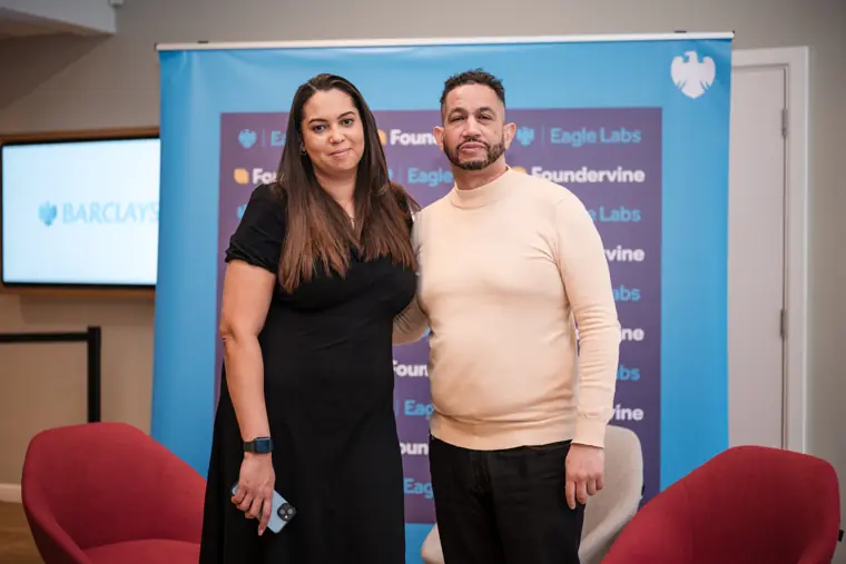 Two attendees pose in front of the event wall.