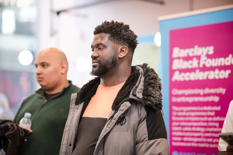 A speaker listens with the Barclays accelerator banner behind him.