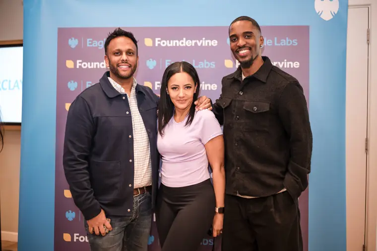 Three people smile together by the event backdrop.