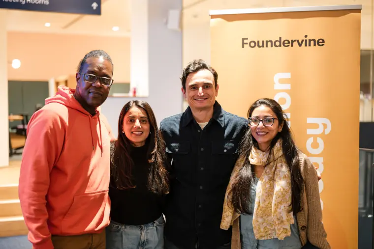 Four attendees smile beside the Foundervine banner.