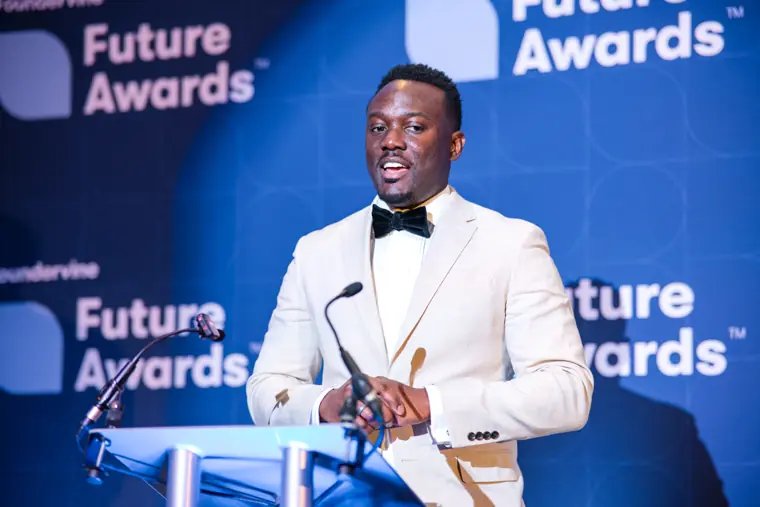 A presenter speaks at the lectern in a white jacket.