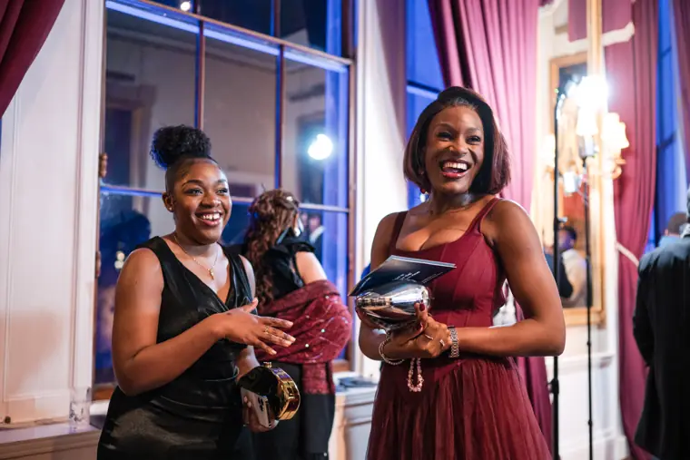 Two attendees smile while holding awards programmes.