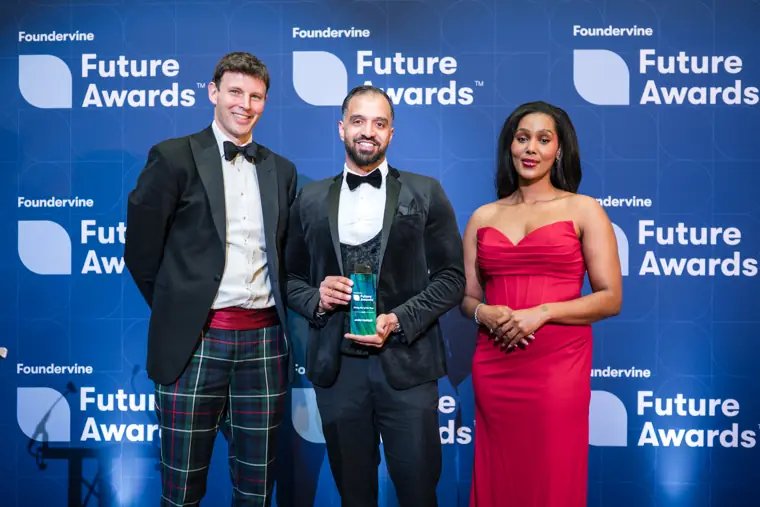 A winner poses with a trophy and presenters.