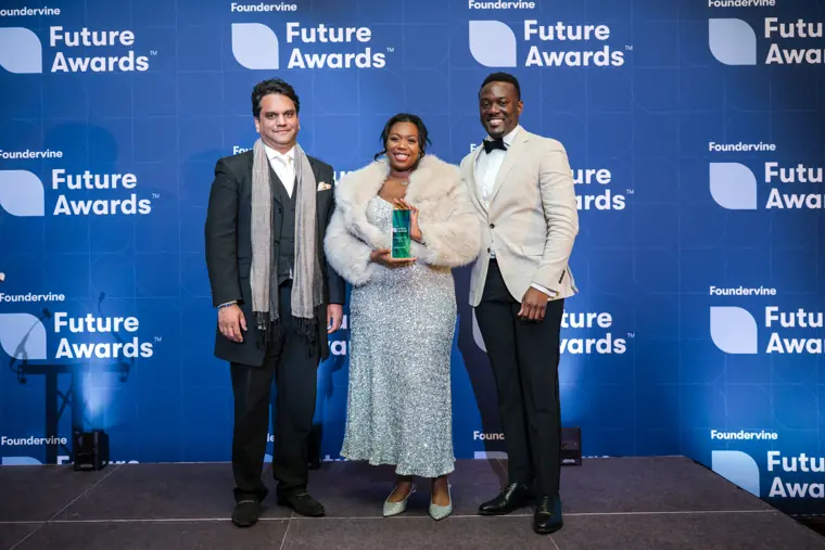 A recipient poses with two presenters and a trophy.