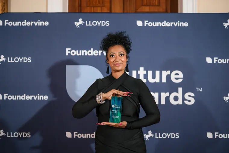 A guest holds an award in front of the Foundervine backdrop.