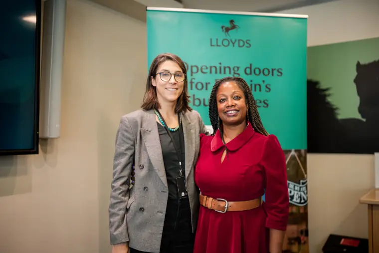 Two attendees smile for a photograph beside the Lloyds banner.