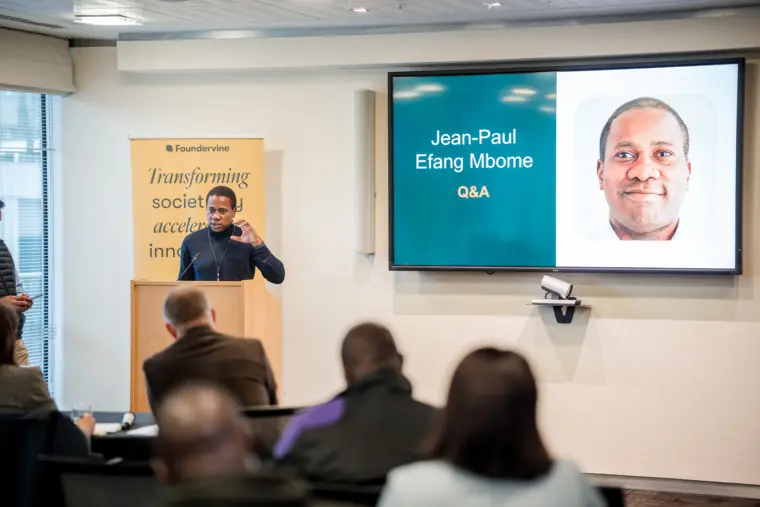 The audience listens as a founder's profile appears on screen.