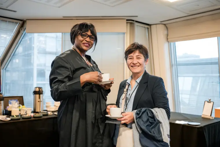 Two attendees meet over refreshments by the venue windows.