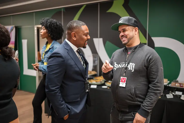Two guests chat in front of the green wall.
