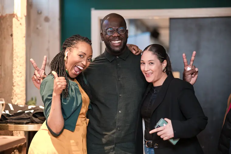 Three guests smile together at the mixer.