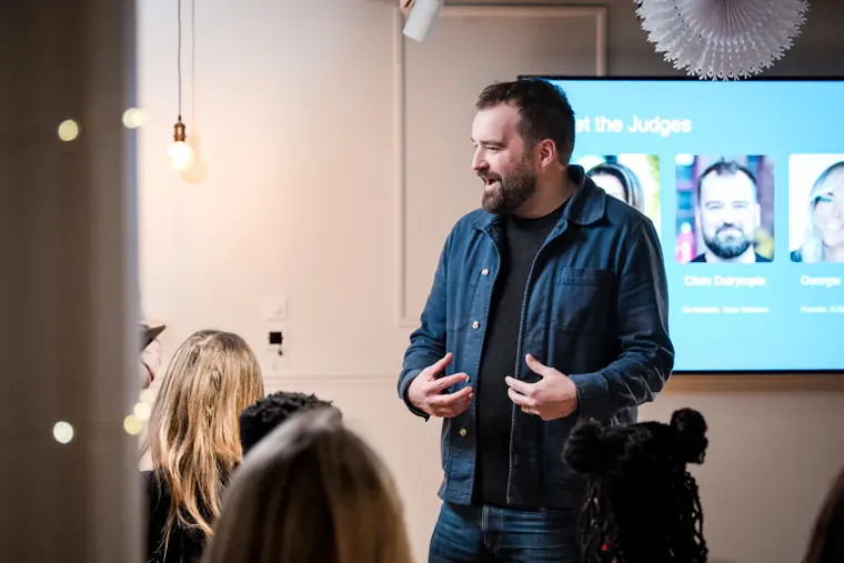 A founder speaks beside the event screen.