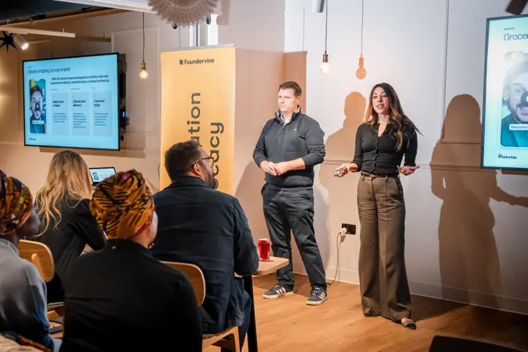 Two speakers stand beside the presentation screen.