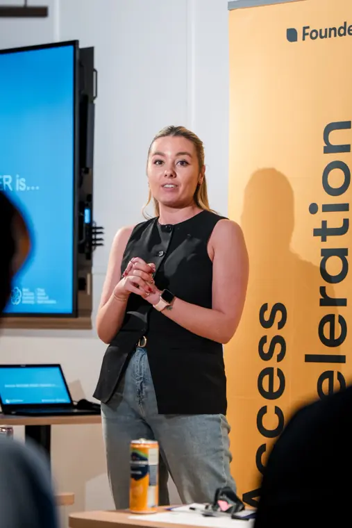 A founder presents beside her slides.