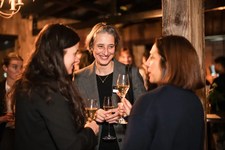 Three women talk together by the wall.