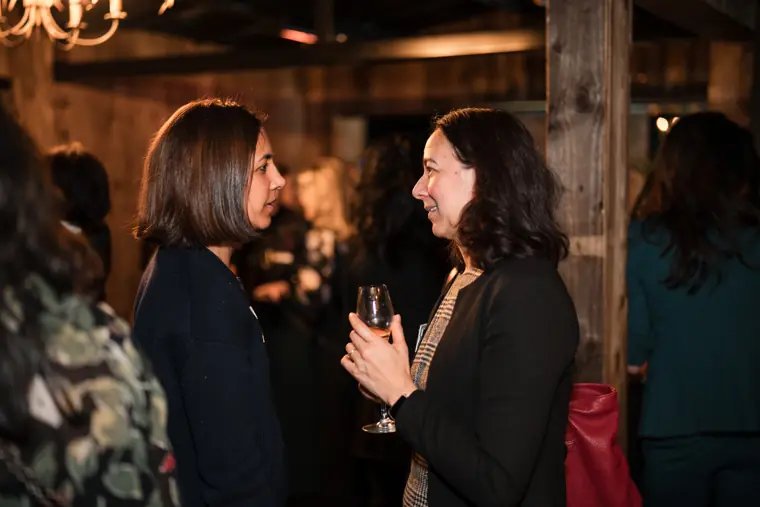 Two attendees speak beside the timber wall.