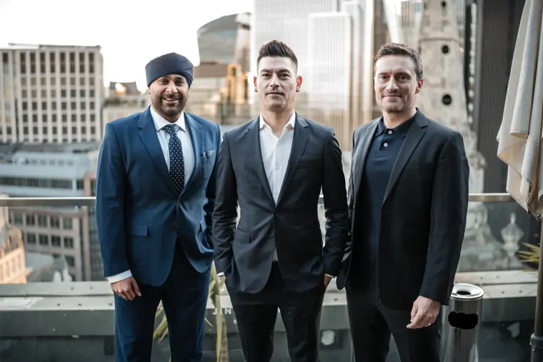 Three colleagues photographed with the London skyline behind them.