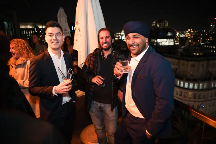 Three guests posing with drinks on the rooftop.