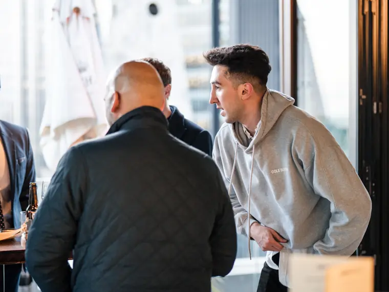 A guest in a light sweater talking with team members.