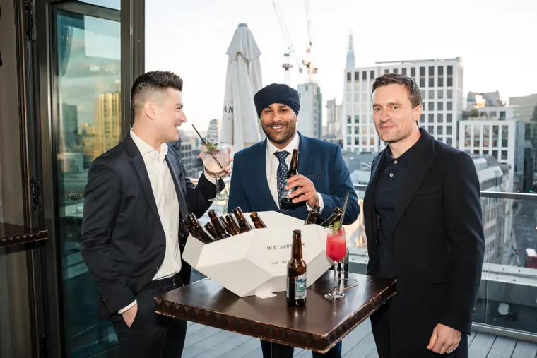 Three colleagues standing together by the rooftop table.