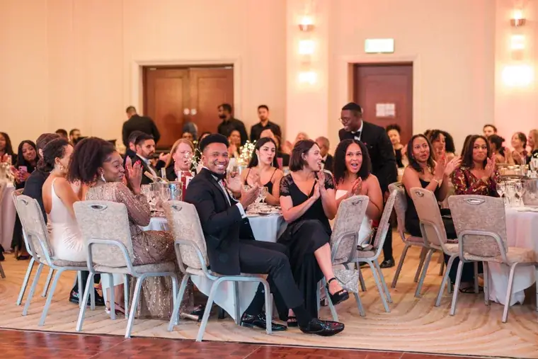 Audience members smiling and applauding from their tables at the Black Pharma fifth anniversary gala.
