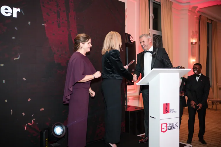 Award recipient shaking hands with a presenter on stage at the Black Pharma fifth anniversary gala.