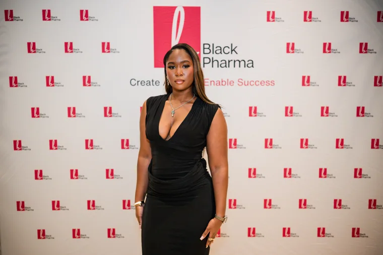 Guest in a black dress posing against the branded backdrop at the Black Pharma fifth anniversary gala.