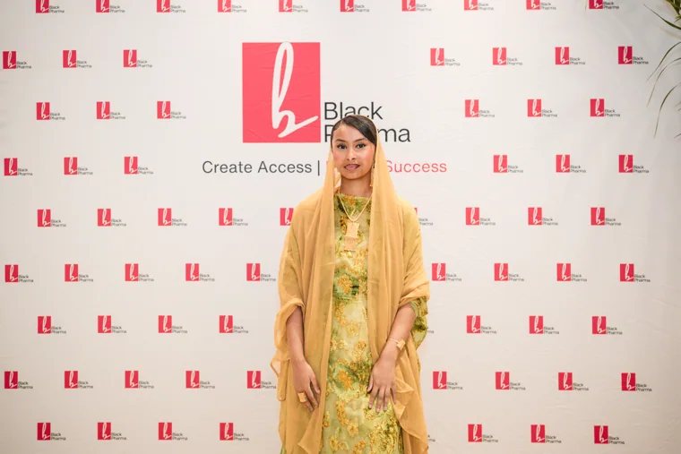 Guest in a gold outfit posing against the gala backdrop at the Black Pharma fifth anniversary gala.