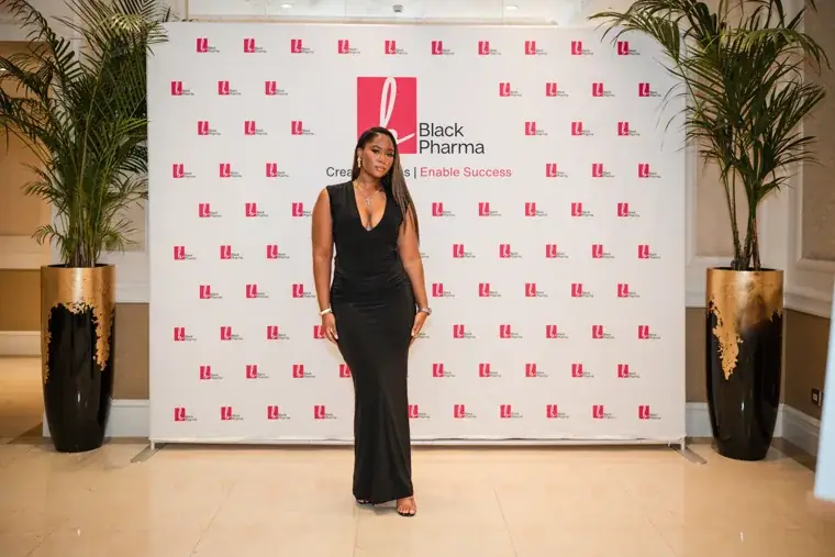 Guest posing in front of the Black Pharma photo wall at the Black Pharma fifth anniversary gala.