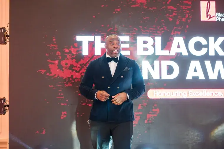 Host standing in front of the anniversary stage screen at the Black Pharma fifth anniversary gala.