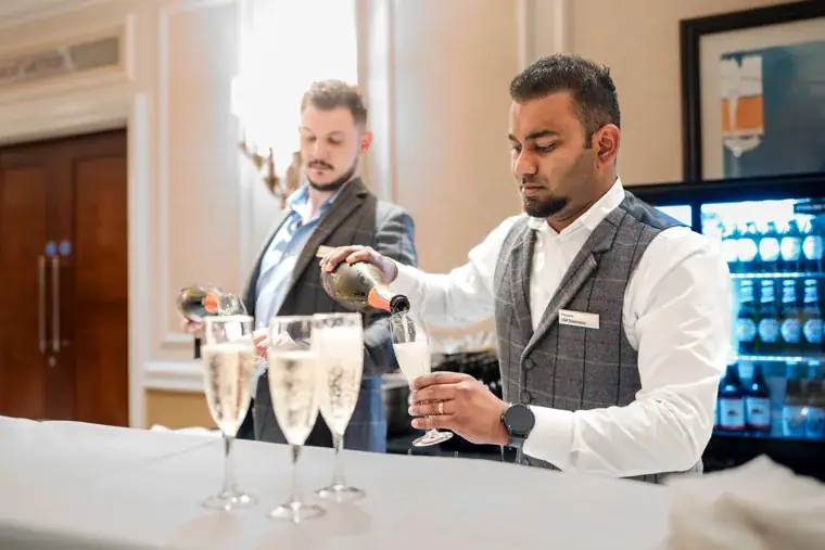 Server pouring sparkling wine for arriving guests at the Black Pharma fifth anniversary gala.