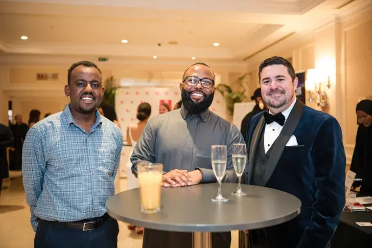 Three men smiling together at a drinks table at the Black Pharma fifth anniversary gala.