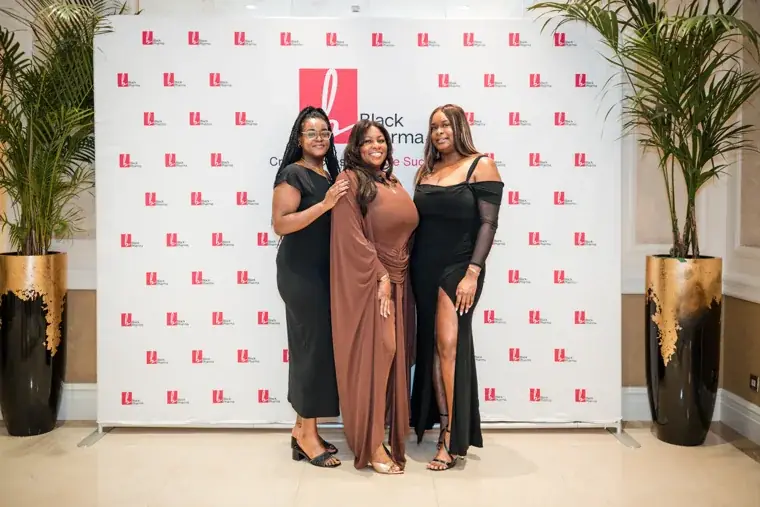 Three women posing together at the photo wall at the Black Pharma fifth anniversary gala.