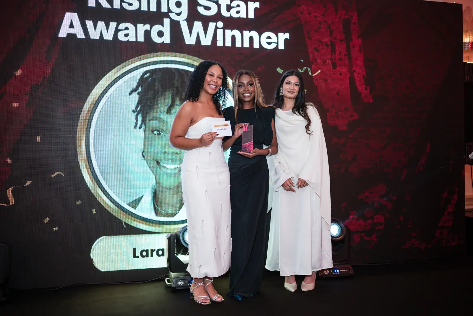 Three women posing with a Rising Star award on stage at the Black Pharma fifth anniversary gala.