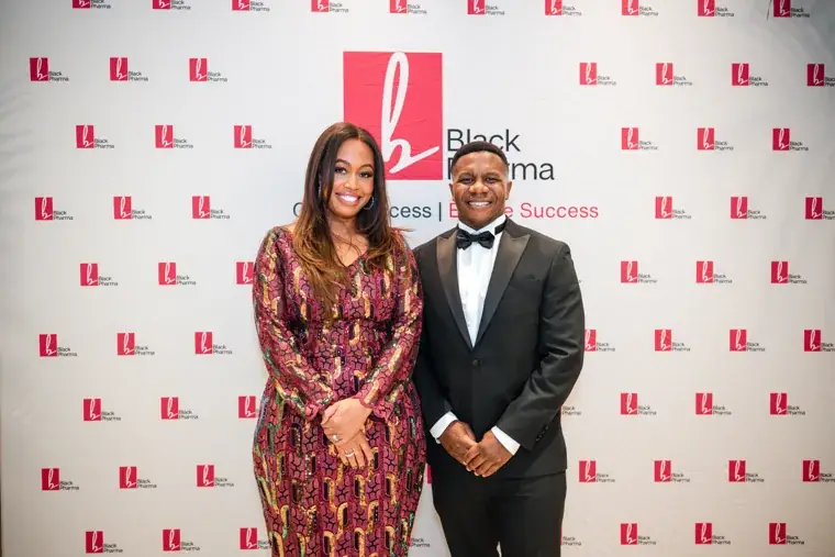 Two guests posing together at the branded photo wall at the Black Pharma fifth anniversary gala.