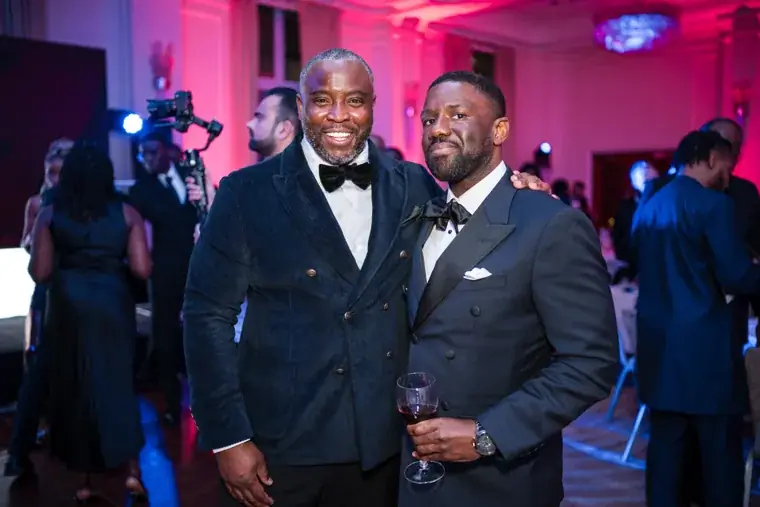 Two men smiling together beside the gala stage at the Black Pharma fifth anniversary gala.