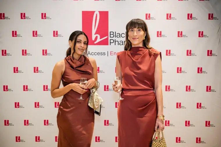 Two women talking in front of the Black Pharma backdrop at the Black Pharma fifth anniversary gala.