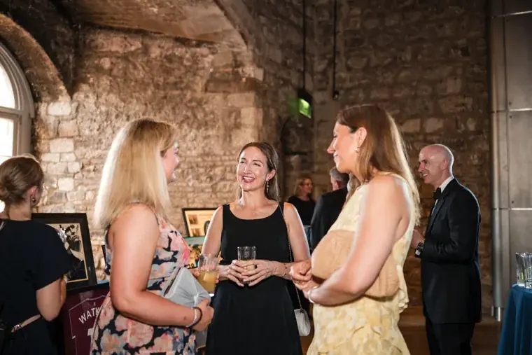 Guests chatting around a drinks table beside the stone wall at the Chambers High Net Worth Awards 2025.
