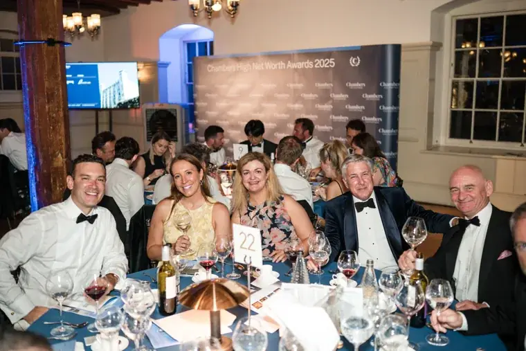 Guests smiling together at their table beneath blue event lighting at the Chambers High Net Worth Awards 2025.